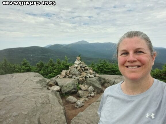 Woman standing in front of a pile of small rocks, mountain range in background