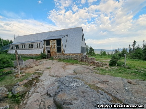 long, low building with light colored walls and windows, mountains and sky in background