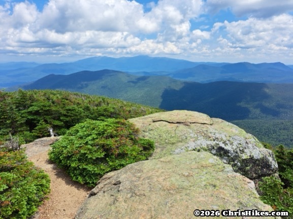 Mountain summit with large smooth rocks, blue mountain range in background