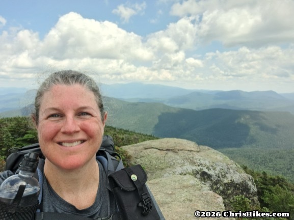 Woman standing on rocky summit with mountain range in background