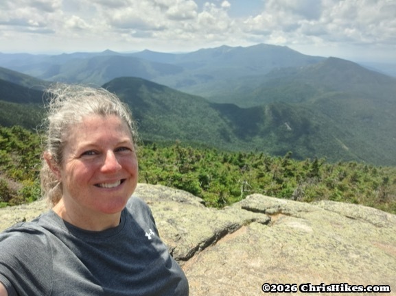 Woman standing on rocky mountain summit with mountain range in background