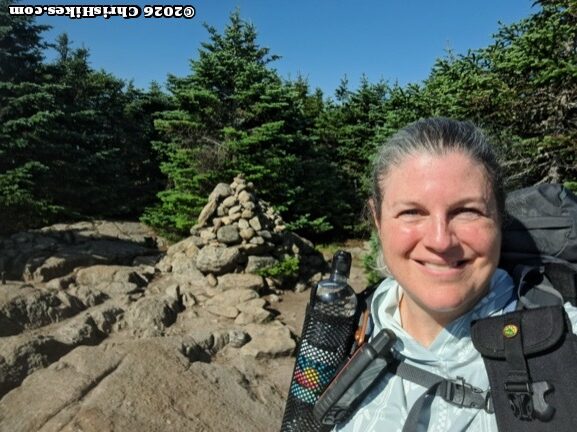 Woman standing in front of a pile of rocks, evergreen trees in background