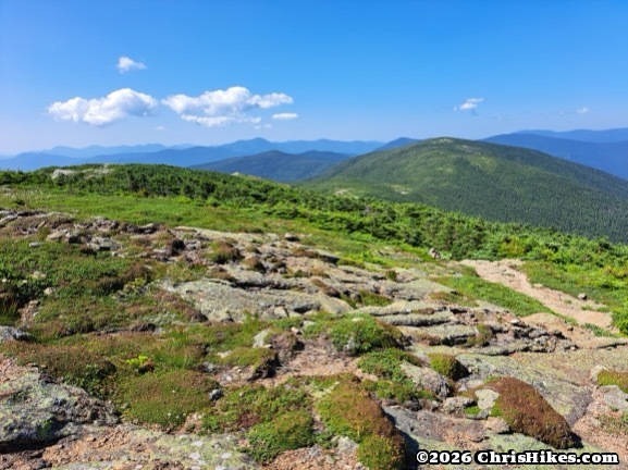 Hiking trail stretching across a treeless summit, green round mountains in background