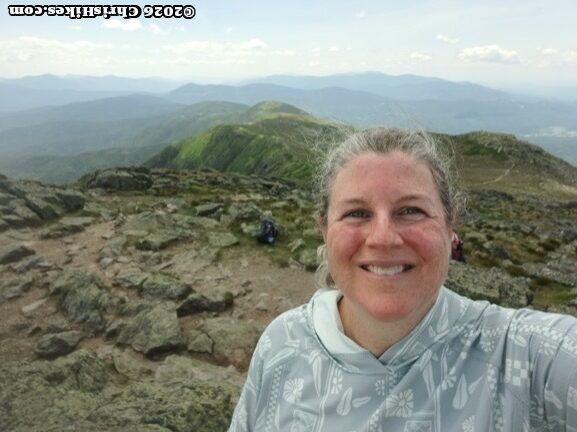 Selfie of woman with rocky and green mountain tops in background