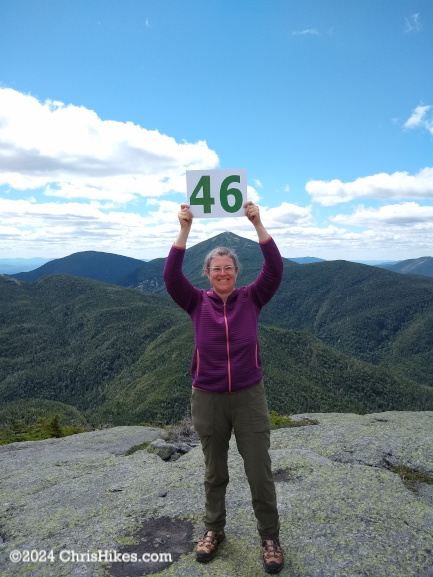 Woman on a mountain summit holding a sign.