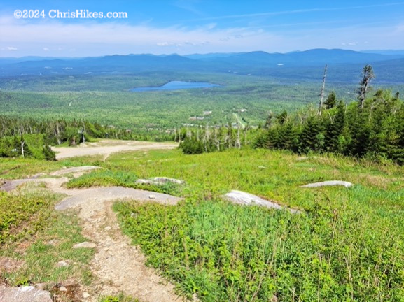 View looking down a ski trail with green grass and distant mountains