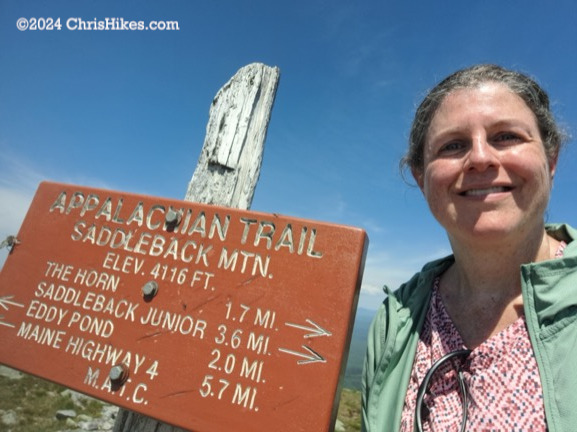 Photograph of person next to mountain summit sign