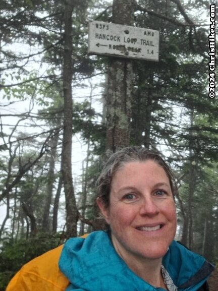 photograph of woman in evergreen forest with white sign in background