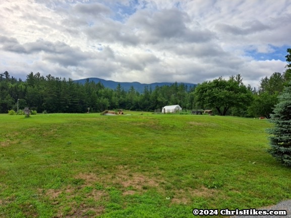 photograph of green field with greenhouse and mountains in the distance.