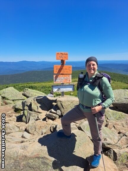 photograph of person standing on rocks in front of a brown sign