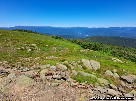 photograph of mountain summit with no trees, many rolling green mountains in the background.