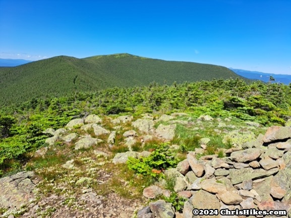 photograph of rocks on a mountain summit with another green summit in the background